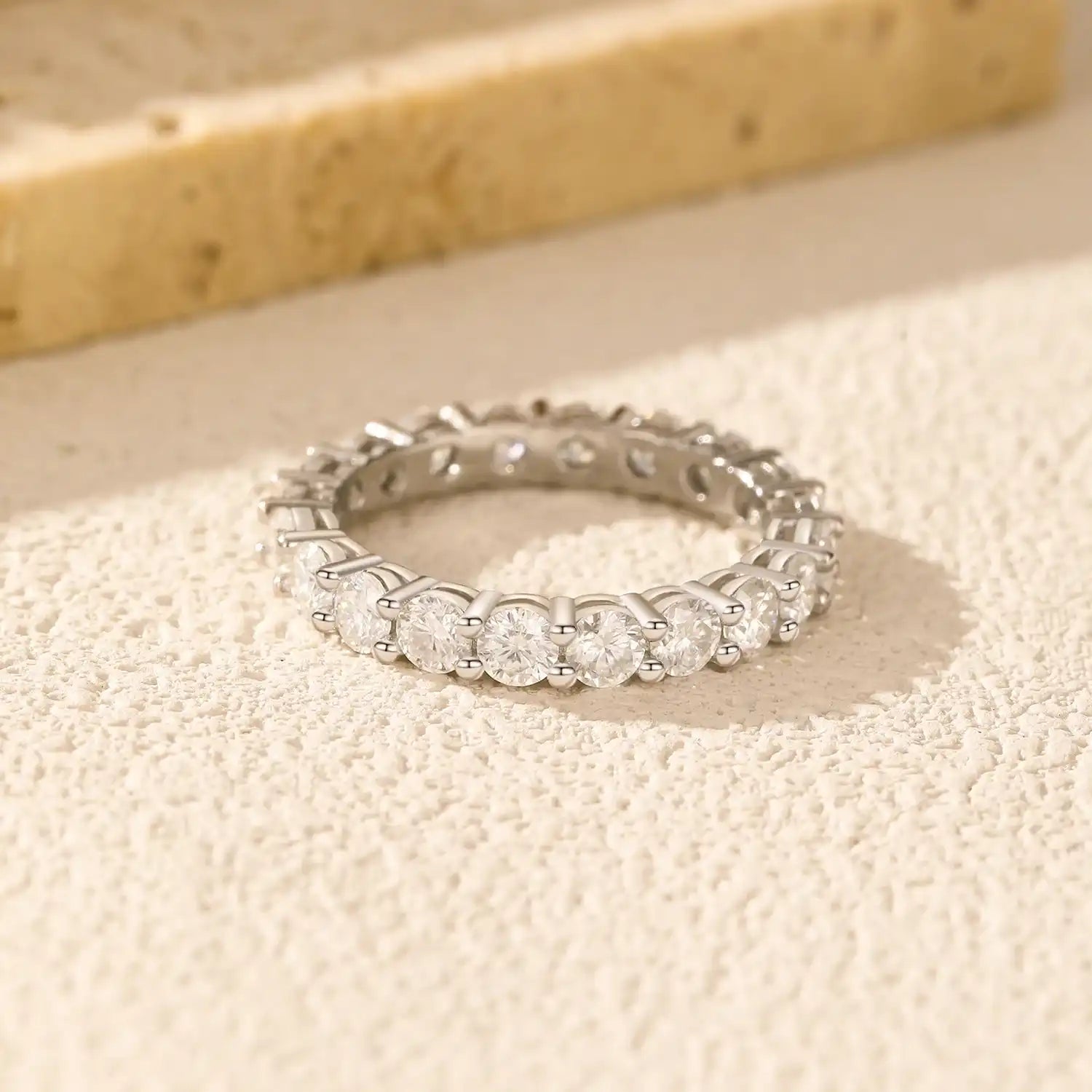 Moissanite eternity band with round stones in silver setting on textured beige surface