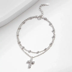 Double-layered silver anklet with moissanite cross pendant on white background
