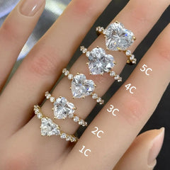 Hand wearing gold moissanite rings with heart-shaped stones in various carat sizes, labeled 1C to 5C.