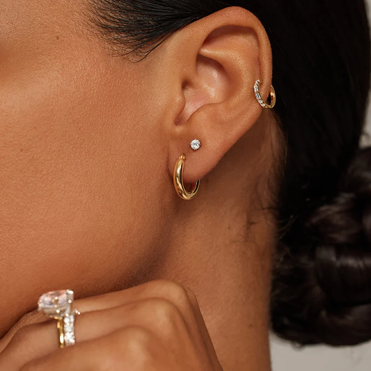 Woman wearing gold hoop earrings, moissanite stud earring, gemstone ring, and diamond hoop