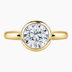 Round bezel moissanite engagement ring with a polished 2.6mm yellow gold band
