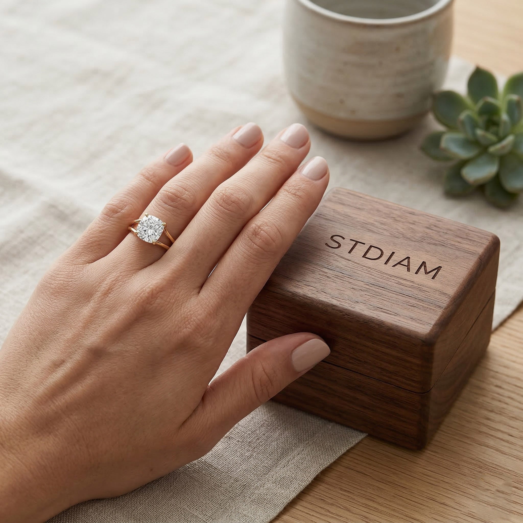 Hand wearing gold moissanite ring beside wooden jewelry box on neutral table setting