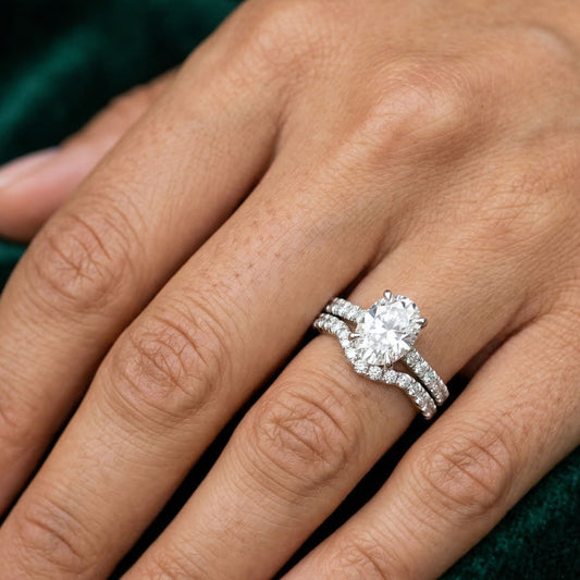 Oval moissanite engagement ring with pavé band and matching wedding band on hand