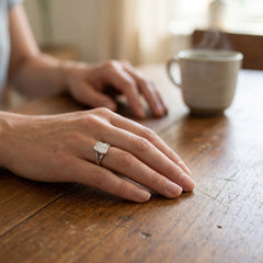 Emerald cut moissanite solitaire ring on hand, natural light, next to a coffee cup
