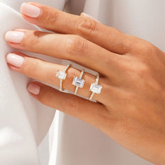 Hand wearing three gold moissanite rings with rectangular stones and pavé bands
