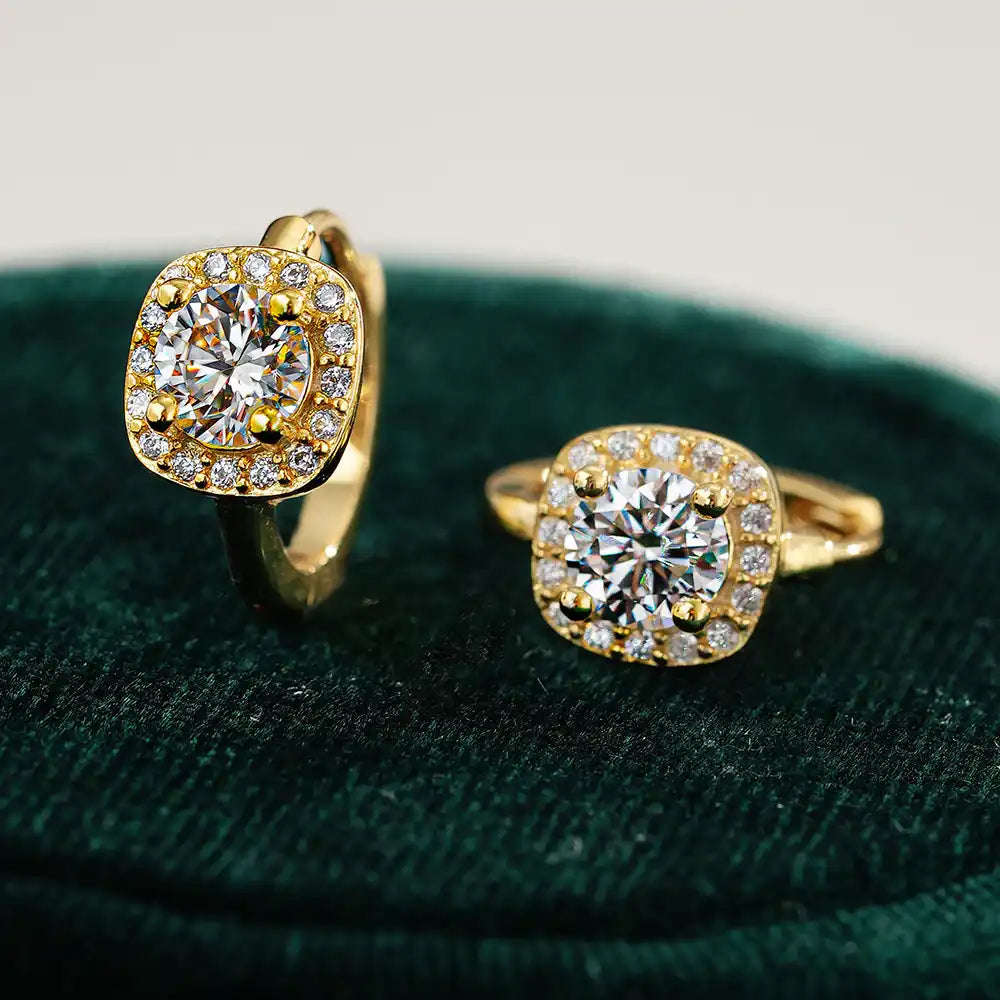Two gold moissanite halo rings with round stones on a dark velvet surface