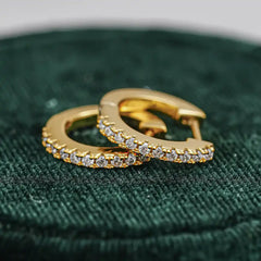 Gold hoop earrings with moissanite stones on green velvet background