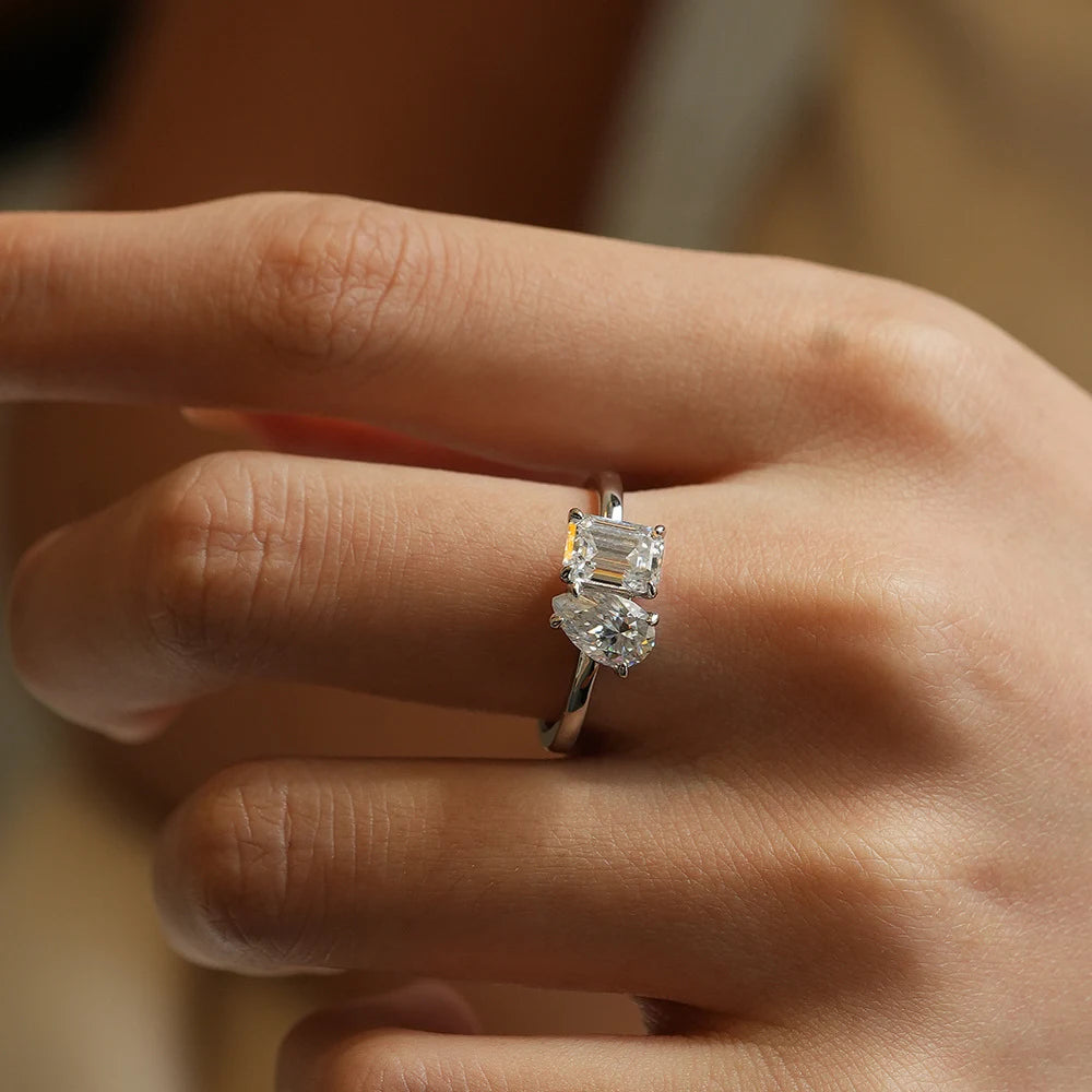 Close-up of a hand wearing a moissanite engagement ring with emerald and pear-cut stones