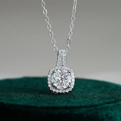 Round moissanite halo pendant necklace in silver with pavé setting on a green surface