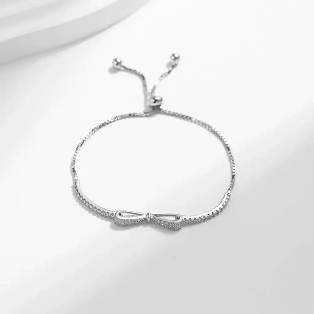 Adjustable silver bow bracelet with sparkling stones on a white background