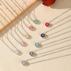 Colorful moissanite gemstone necklaces with silver chains displayed on a textured surface