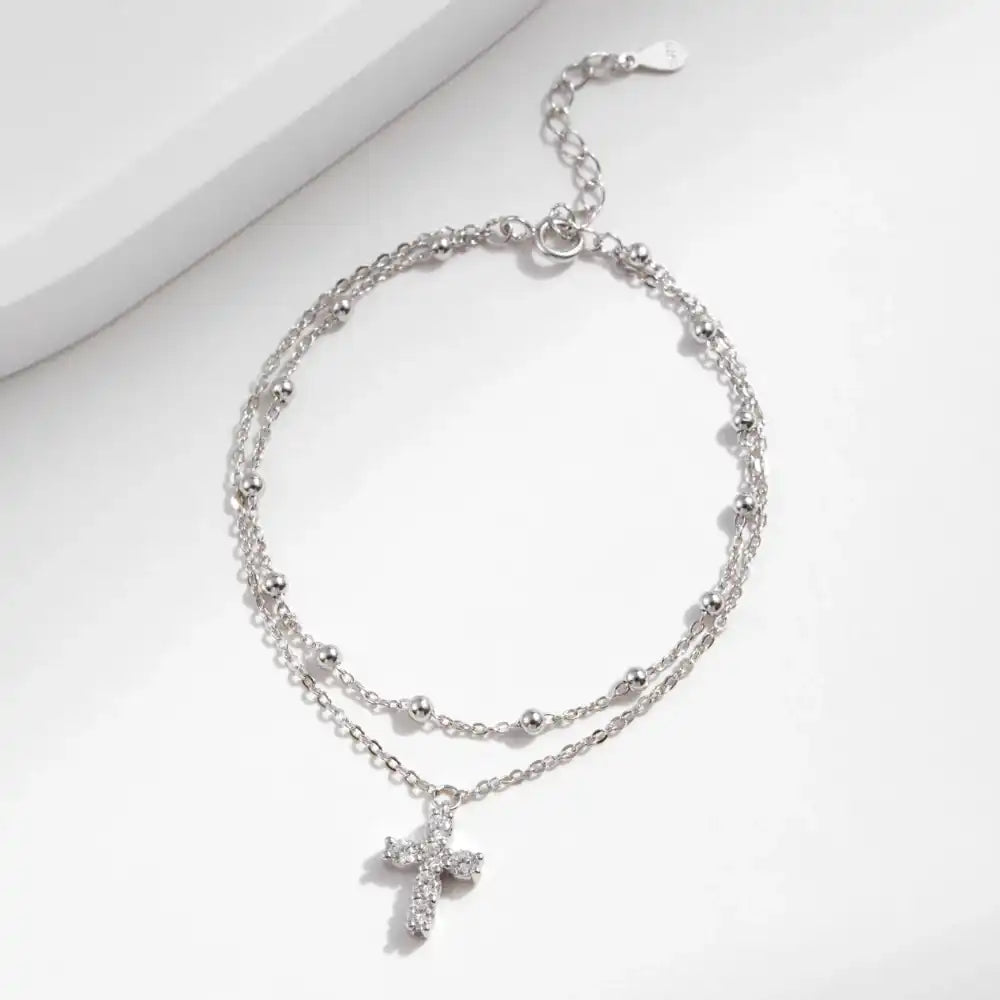 Double-layered silver anklet with moissanite cross pendant on white background