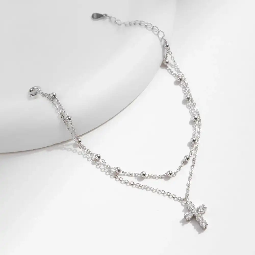 Double-layered silver necklace with moissanite cross pendant and beaded chain on white background.