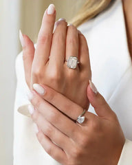Woman wearing emerald-cut moissanite engagement ring and pear-shaped moissanite ring on manicured hands