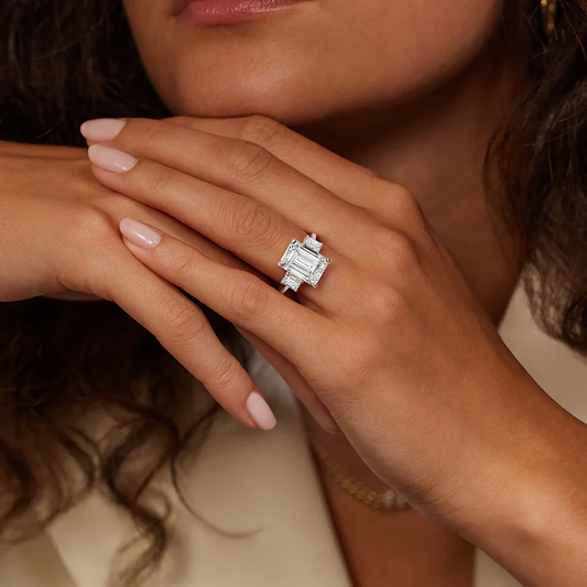 Woman wearing an emerald cut moissanite ring with side stones on her hand
