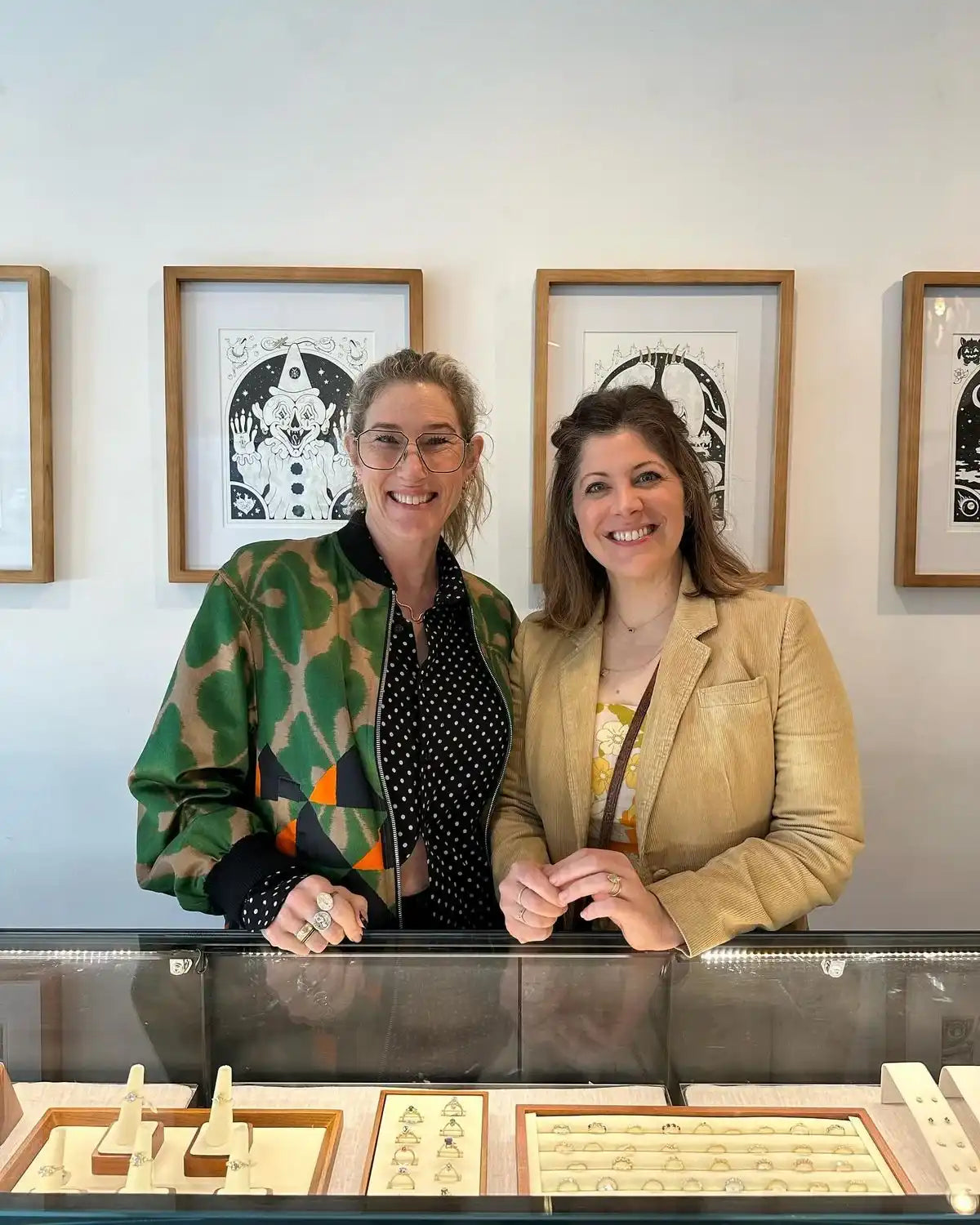 Two women standing behind a jewelry display case with moissanite rings in a modern showroom.