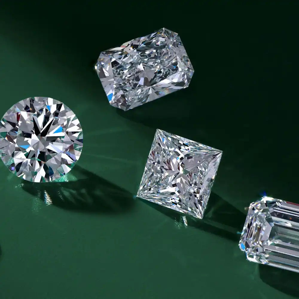 Loose moissanite gemstones in round, princess, emerald, and radiant cuts on green background