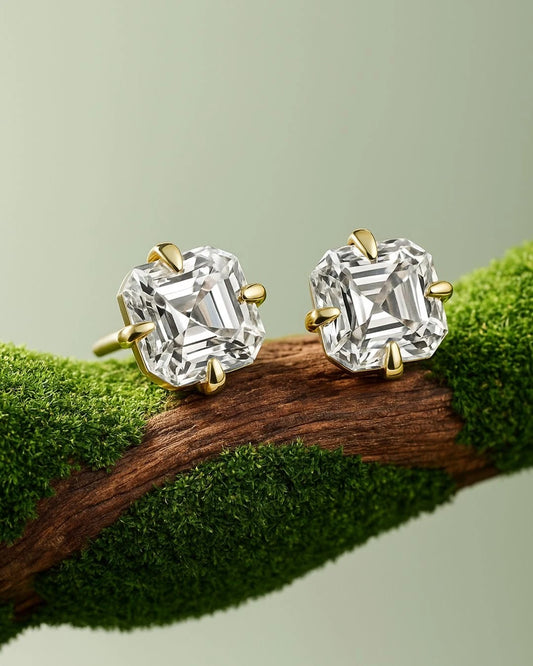 Asscher cut moissanite stud earrings with gold prongs on textured green branch