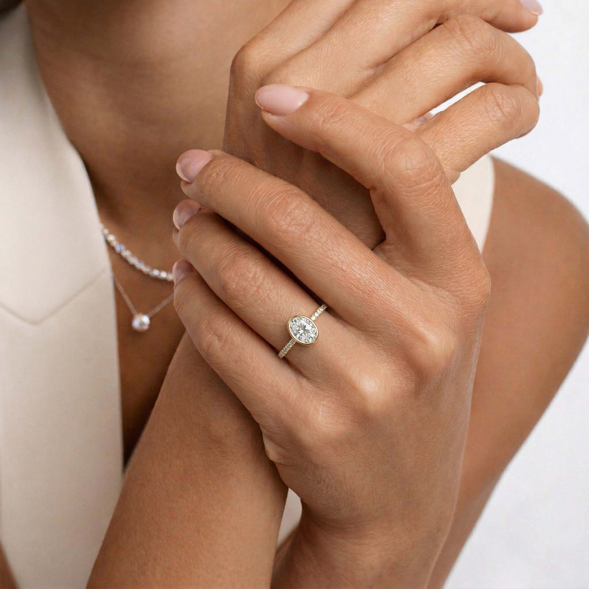 Woman wearing an oval moissanite engagement ring with a gold band and pearl necklace