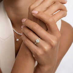 Woman wearing an oval moissanite engagement ring with a gold band and pearl necklace