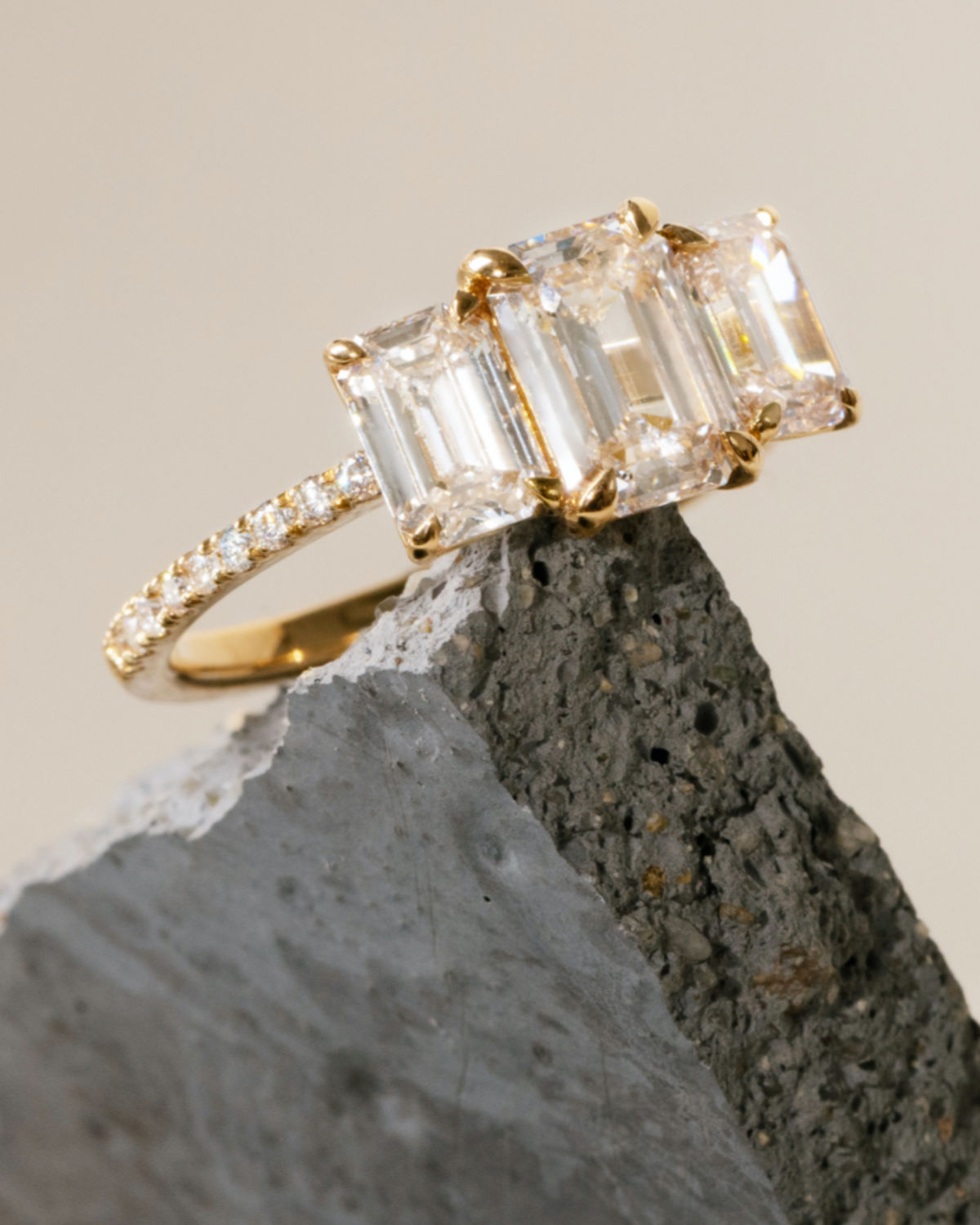 Gold three-stone moissanite ring with emerald cut stones on textured rock, luxury jewelry