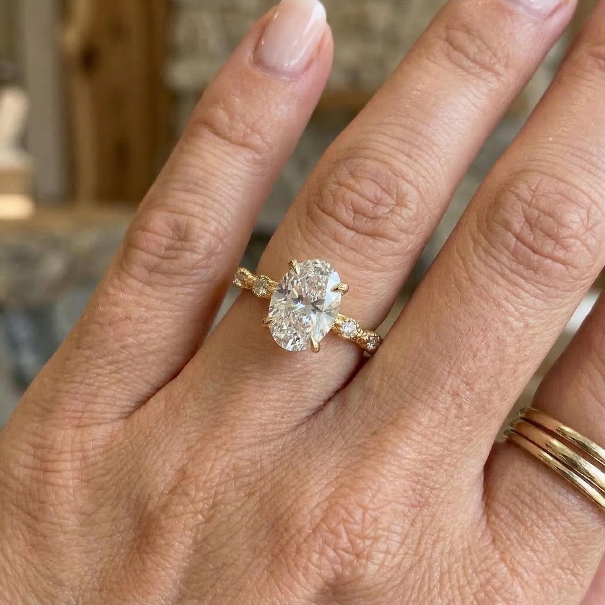 Oval moissanite engagement ring with gold band and side stones on hand