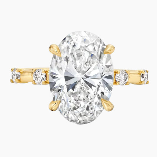 Oval moissanite engagement ring with gold band and side stones on white background