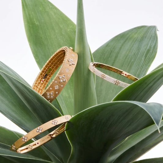 Gold moissanite bangles with floral designs displayed on succulent leaves