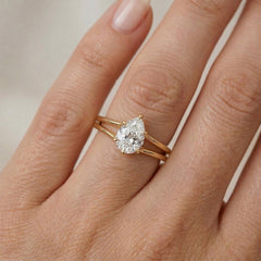 Pear cut moissanite engagement ring with gold band on hand