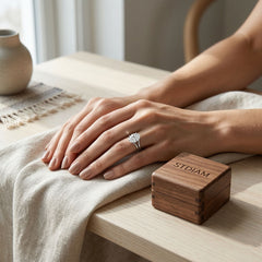 Woman's hand wearing a premium moissanite engagement ring near a wooden ring box