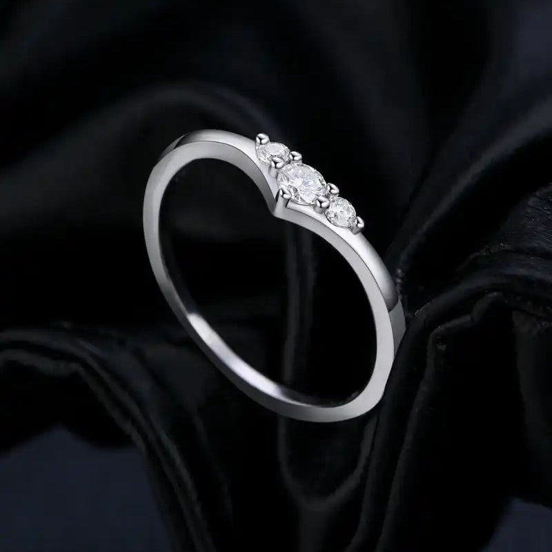 Heart-shaped silver ring with three moissanite stones on black fabric