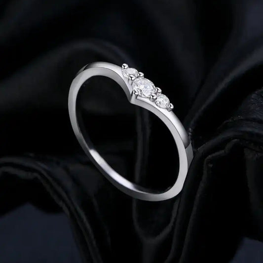 Heart-shaped silver ring with three moissanite stones on black fabric