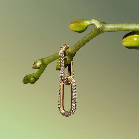 Gold link moissanite earring with pave stones hanging on a green plant stem