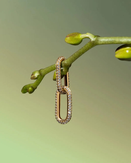 Gold link moissanite earring with pave stones hanging on a green plant stem